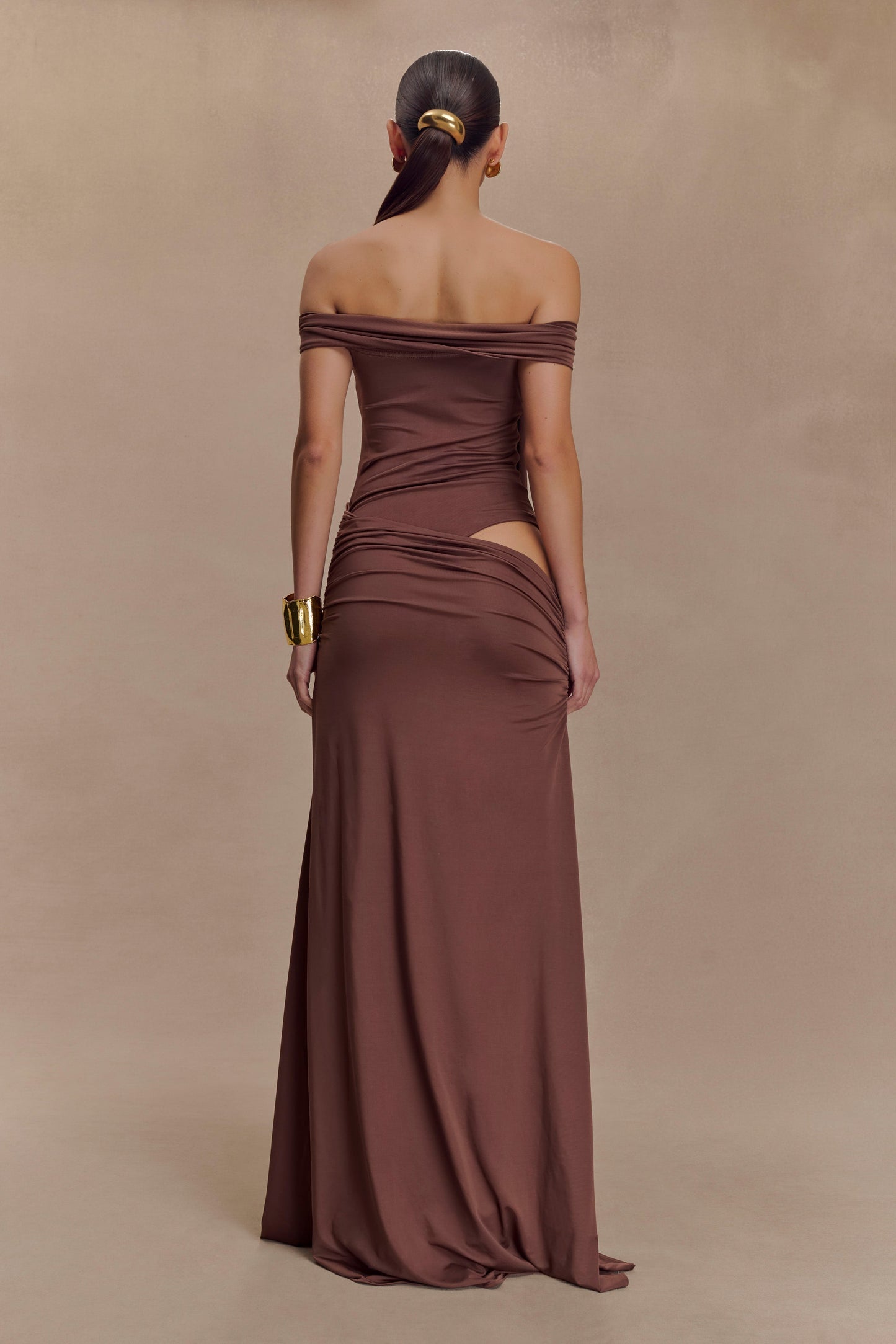 Oliver van Meshki - mochabruine off-shoulder maxi-jurk met cut-out en gouden detail te huur bij POOMBIES, jurk huren voor gala of feest