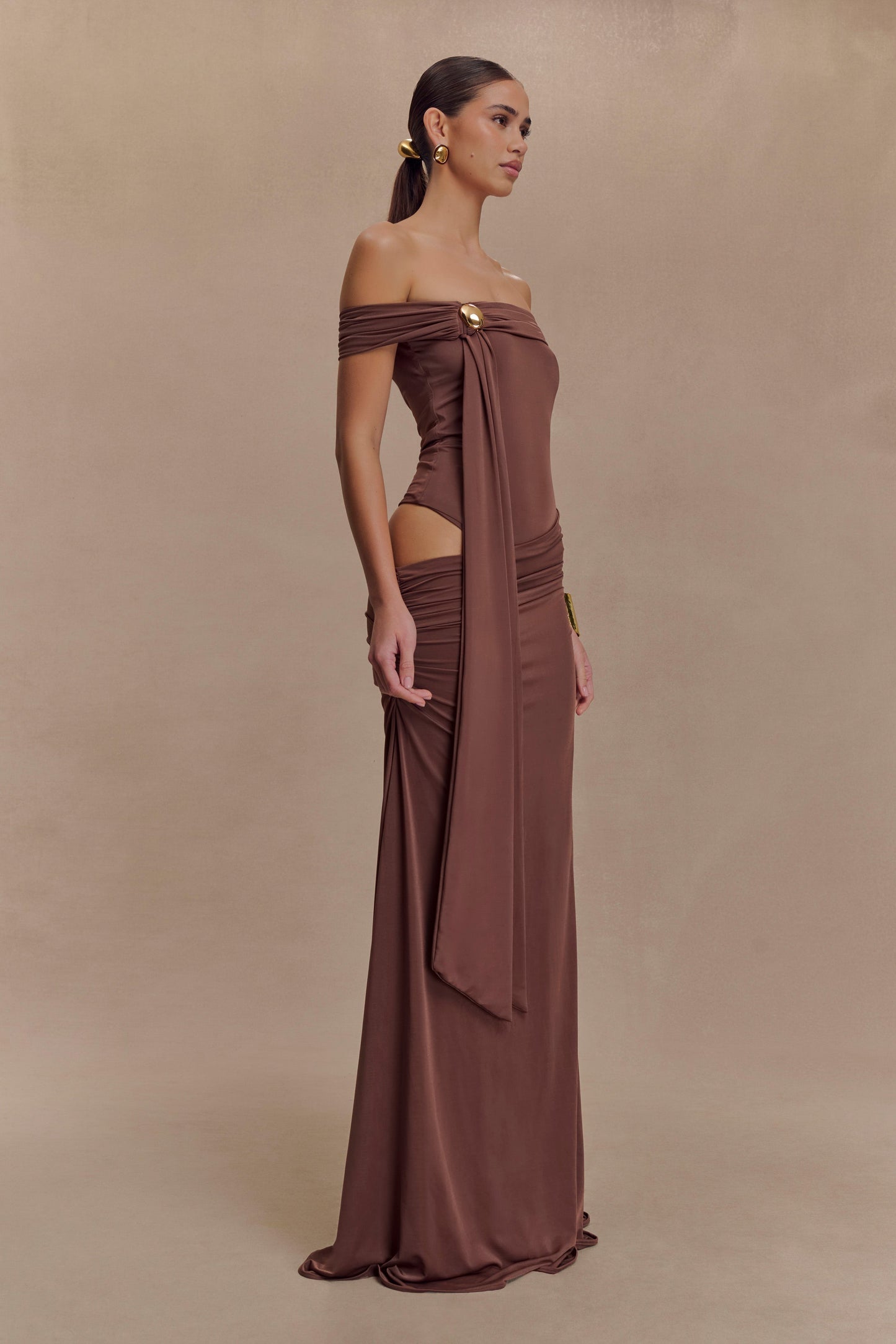 Oliver van Meshki - mochabruine off-shoulder maxi-jurk met cut-out en gouden detail te huur bij POOMBIES, jurk huren voor gala of feest