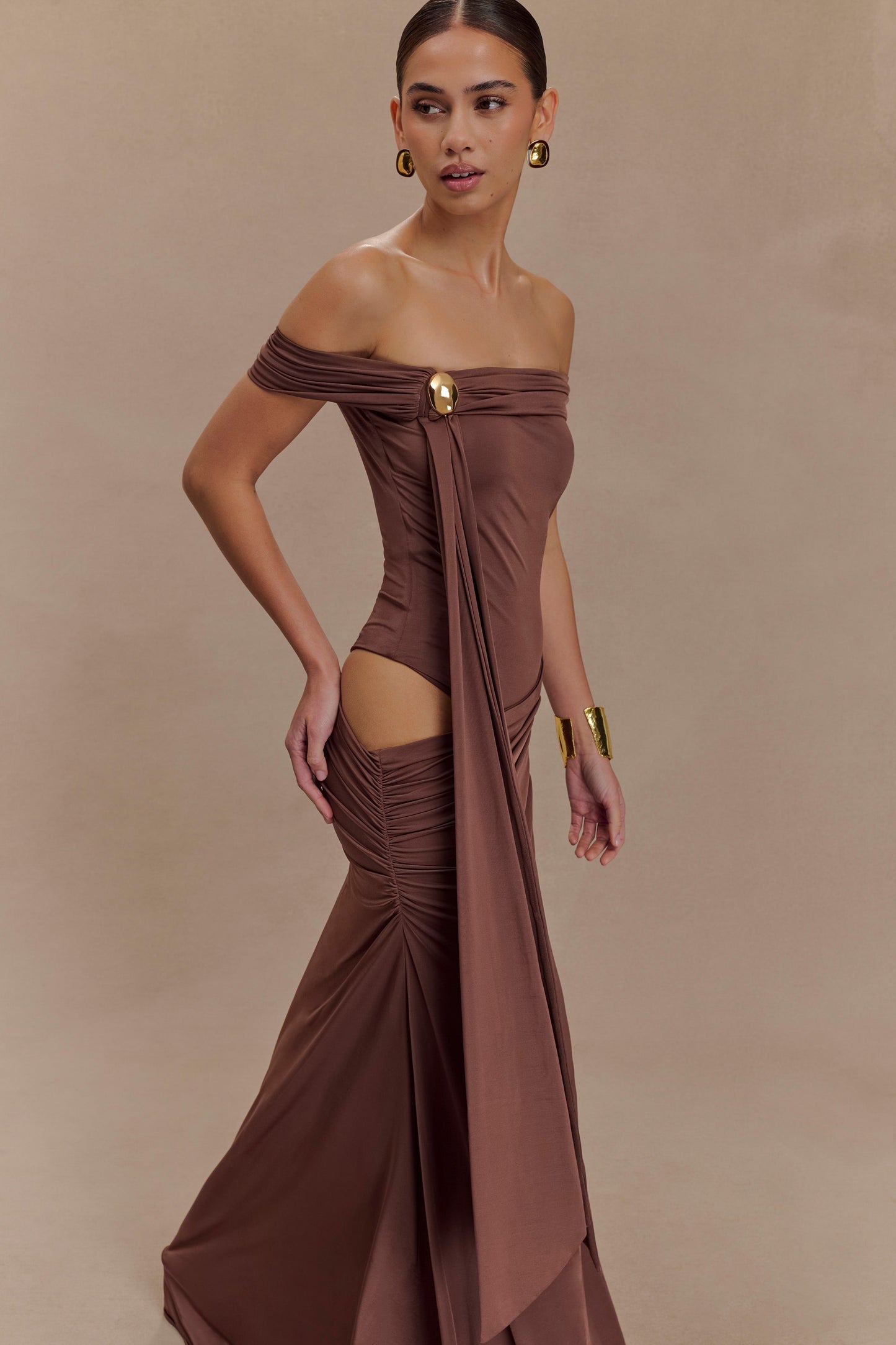 Oliver van Meshki - mochabruine off-shoulder maxi-jurk met cut-out en gouden detail te huur bij POOMBIES, jurk huren voor gala of feest